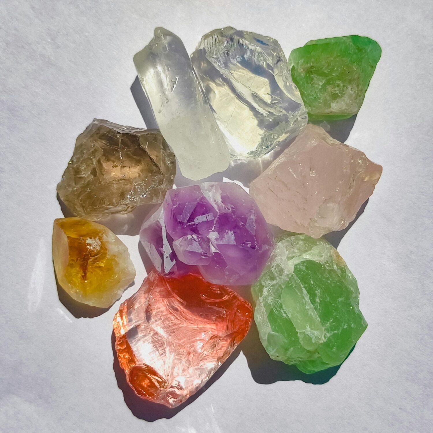 A vibrant collection of colorful crystals arranged in bright sunlight on a white surface.